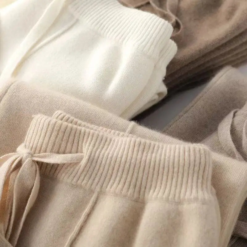 Beige, hvide og brune cashmere bukser i blødt materiale, foldet og stablet. Komfortable og stilfulde bukser til vintermode.