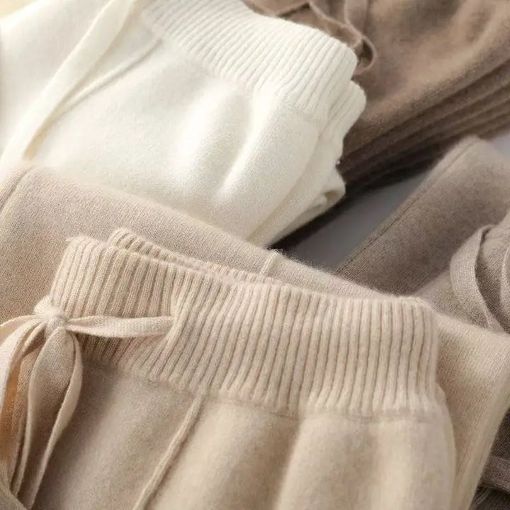Beige, hvide og brune cashmere bukser i blødt materiale, foldet og stablet. Komfortable og stilfulde bukser til vintermode.