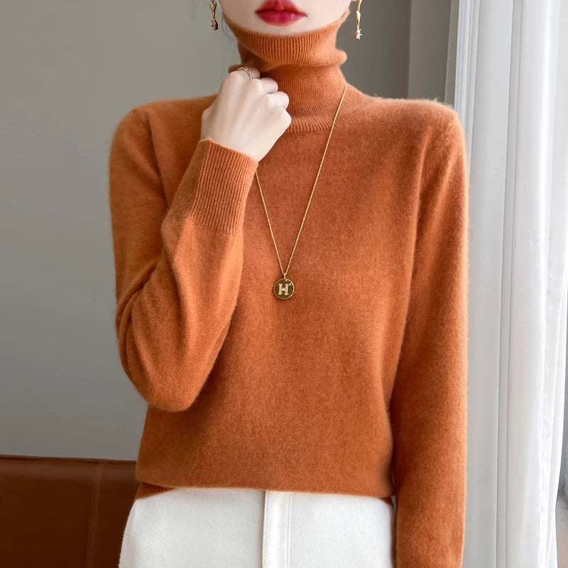 Kvinde iført orange rullekrave sweater, guldhalskæde med "H" vedhæng, og hvide bukser. Elegant efterårslook, moderne mode, stilfuldt outfit.