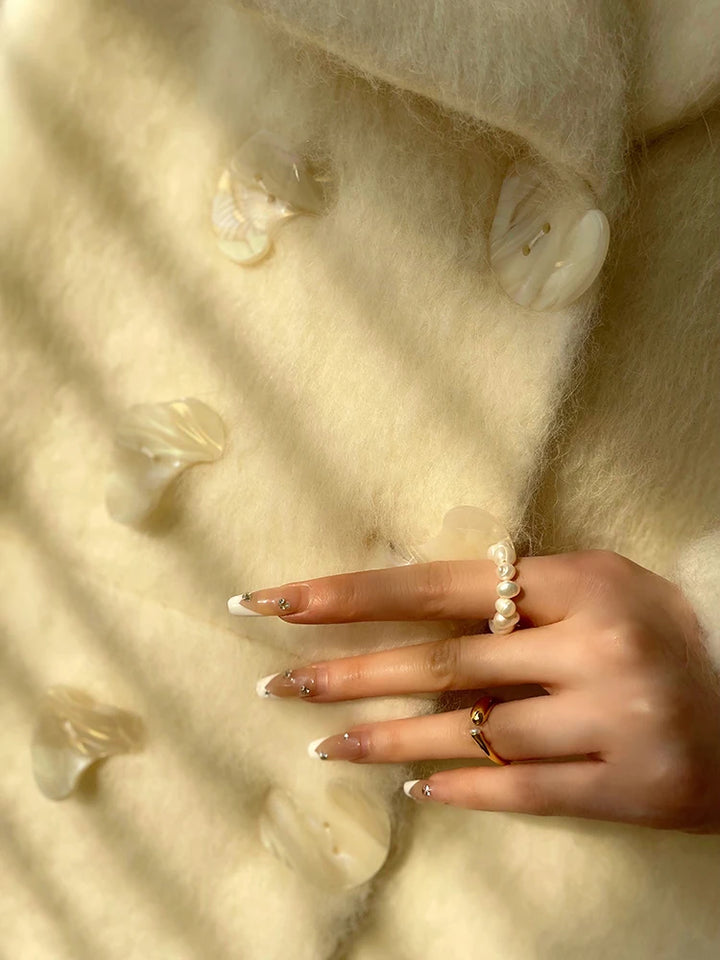 Hånd med fransk manicure og perlering på uldfrakke med store knapper. Elegant mode, vintertøj, stilfuldt tilbehør.