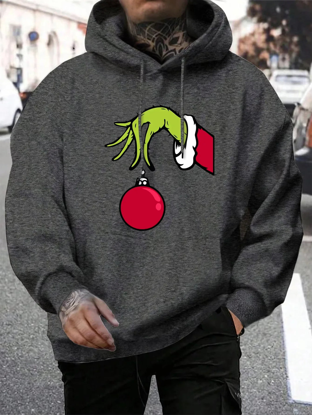 Grå hættetrøje med Grinch-motiv, der holder en rød julekugle. Perfekt til jul, unisex streetwear, komfortabel og stilfuld vintermode.