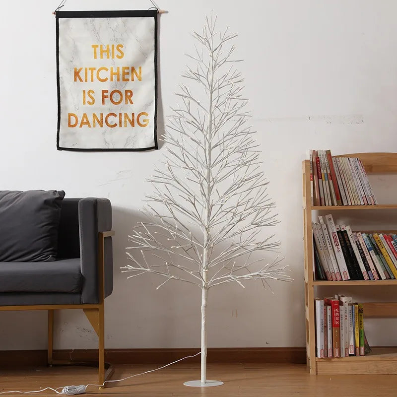 Hvid kunstigt juletræ uden pynt ved siden af en grå sofa og bogreol. Vægdekoration med teksten "This Kitchen is for Dancing".