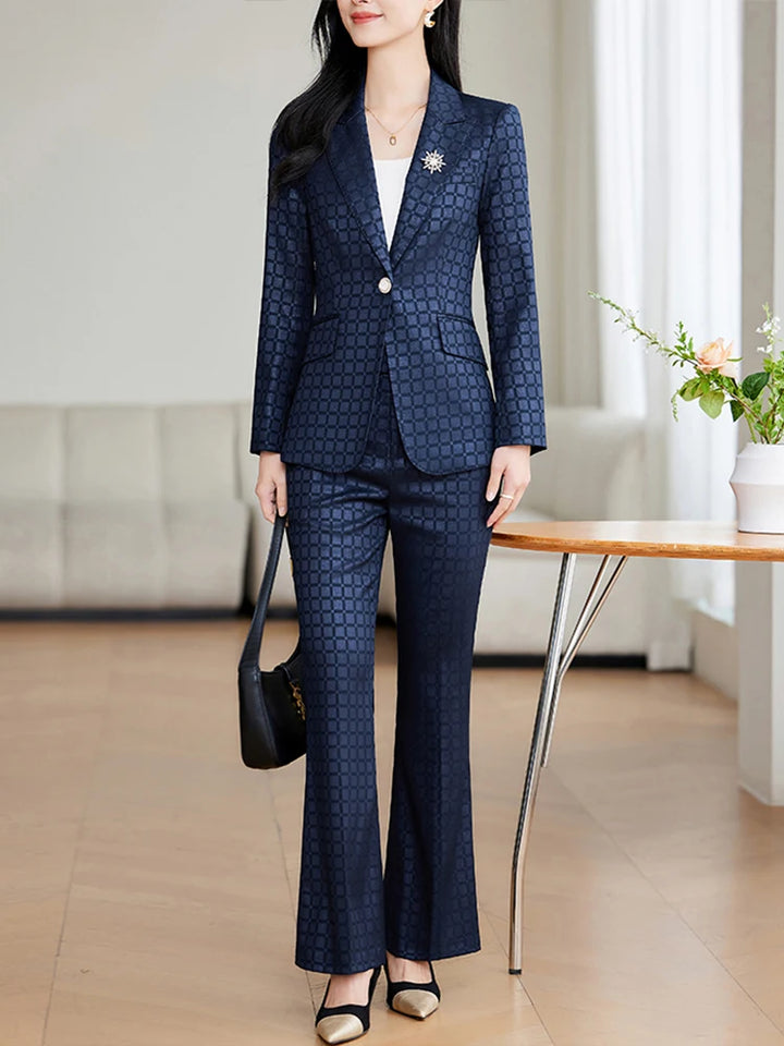 Kvinde i elegant, mørkeblå jakkesæt med mønster, står i moderne stue. Hun bærer sort taske og hvide sko. Perfekt til business og formelle lejligheder.