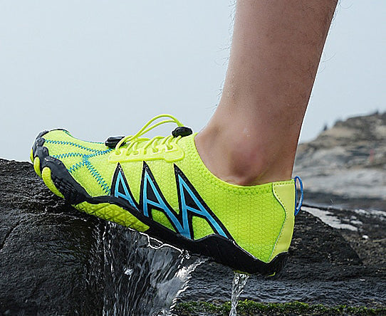 Neongul løbesko med sort og blå detaljer på klippe ved vand. Minimalistisk design, ideel til udendørs sport og vandsport.