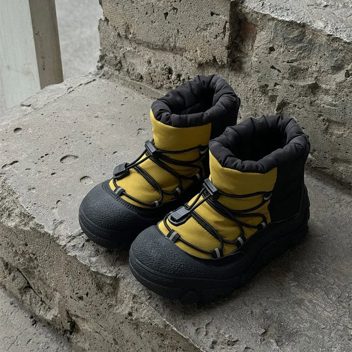Gule og sorte vinterstøvler med snørebånd på betontrappe. Vandtætte børnestøvler, robust design, ideelle til kolde vejrforhold.