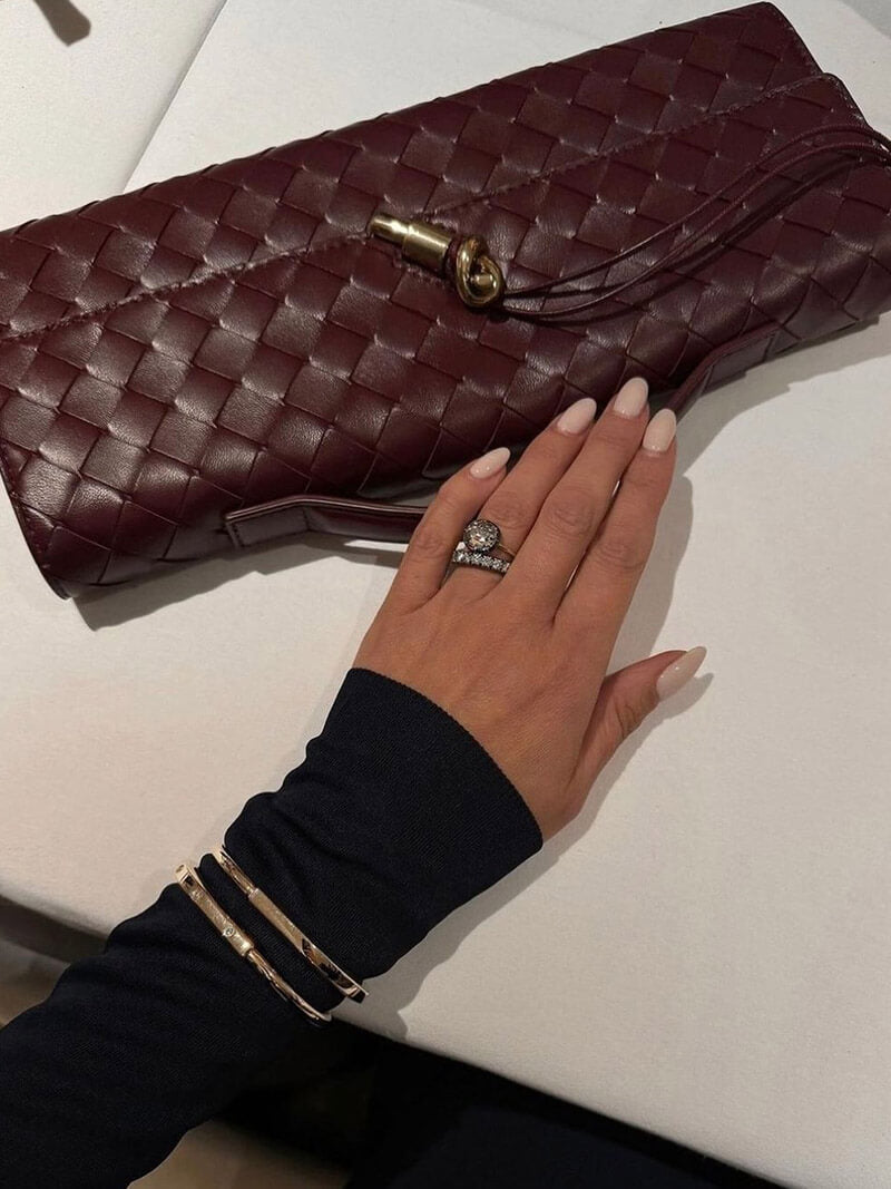 Brun flettet læder clutch på hvid baggrund, hånd med smykker og lyse negle. Elegant modeaccessory, stilfuldt design, kvindelig elegance.