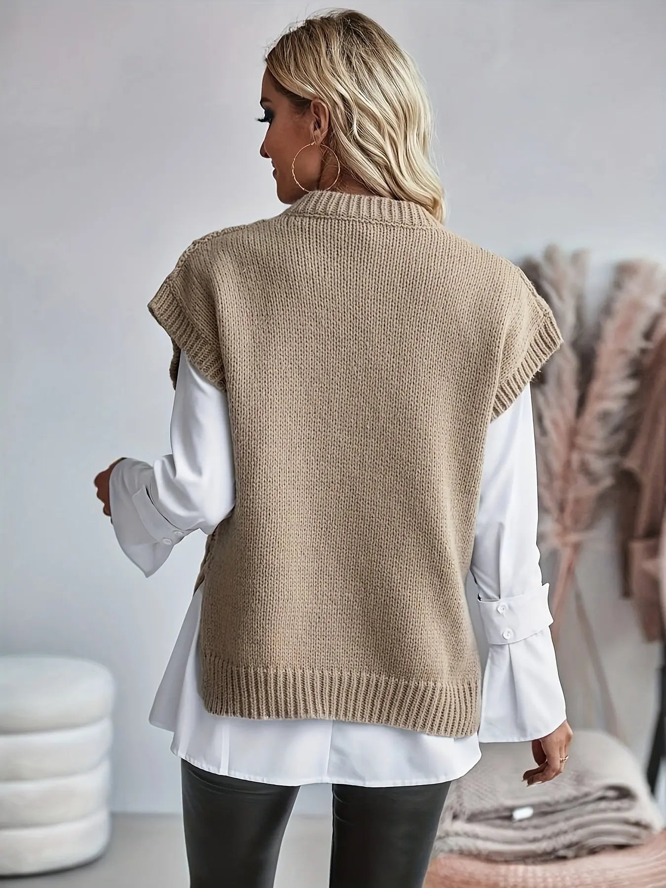 Kvinde iført beige strikvest over hvid skjorte, set bagfra. Moderne mode, afslappet stil, efterårstøj. Perfekt til trendy, stilbevidste kvinder.