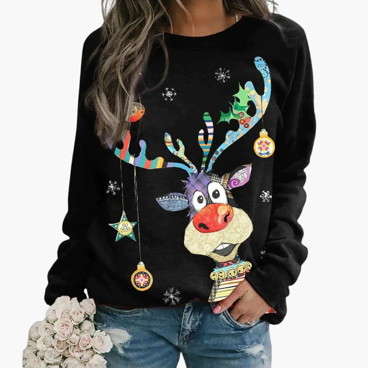 Kvinde iført sort juletrøje med farverigt rensdyrmotiv, holder en buket hvide blomster. Perfekt til julefest, vintermode, unikt design.