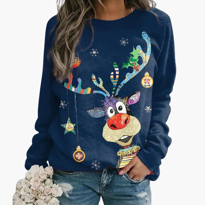 Kvinde iført blå juletrøje med farverig rensdyrgrafik og snefnug, holder en buket hvide blomster. Festlig vintermode, casual look.