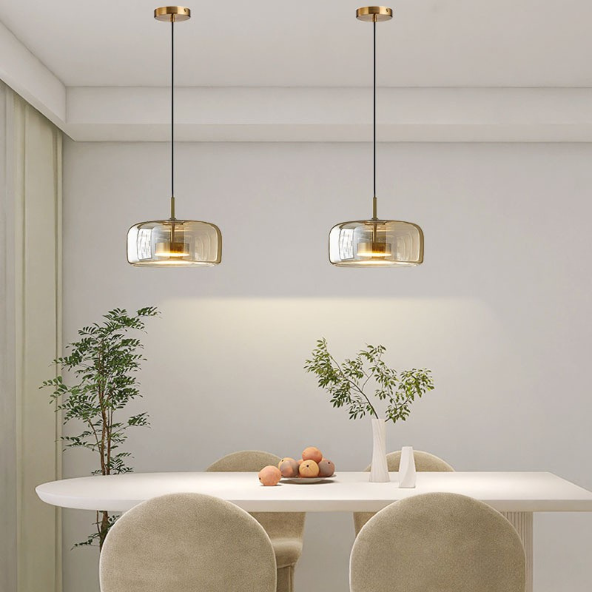 Moderne spisestue med to hængende messinglamper over et ovalt hvidt bord, omgivet af beige stole og dekoreret med friske grene og frugter.