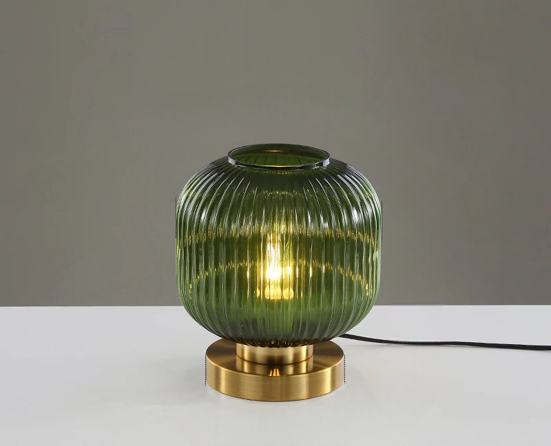 Grøn glasbordlampe med rillet design og gylden base på hvid overflade. Moderne belysning, stilfuldt interiør, dekorativ lampe.