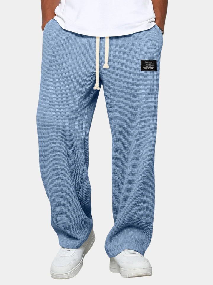 Blå herre sweatpants med snøre, afslappet pasform og sort mærke på venstre lår. Komfortabelt tøj til hverdagsbrug.
