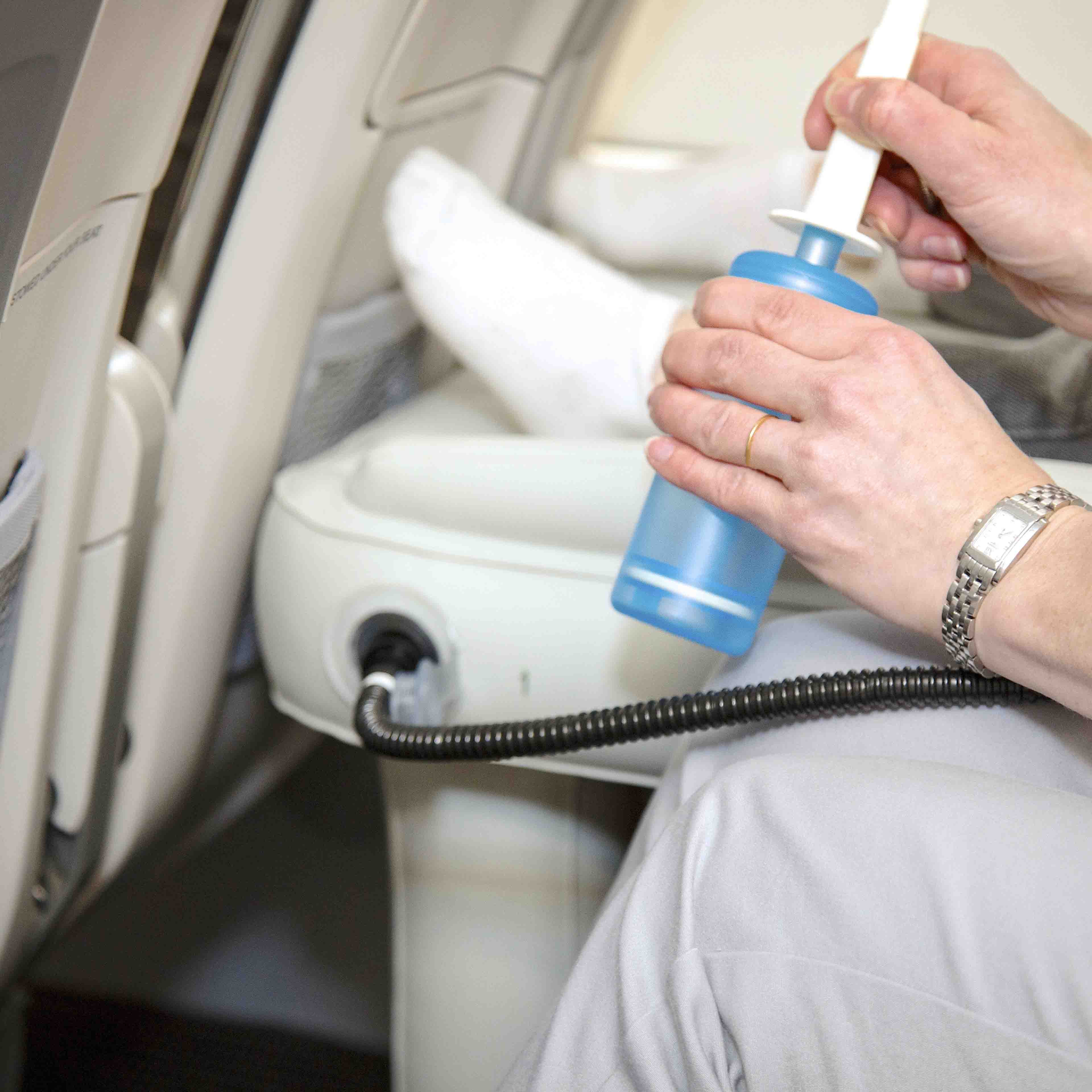 Person bruger en bærbar iltflaske i flysæde. Rejse, sundhed, iltbehandling, flysikkerhed. Hænder holder blå iltbeholder med slange.