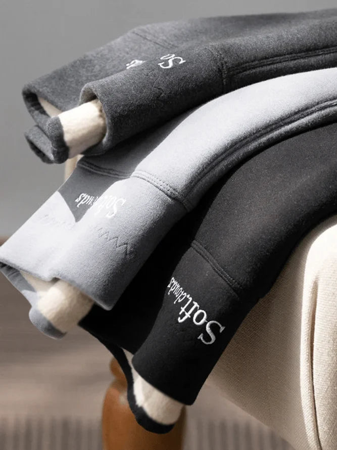 Fire par bløde, fleeceforede leggings i grå og sort, stablet på en stol. Komfortable vinterleggings med elastisk talje og varm foring.