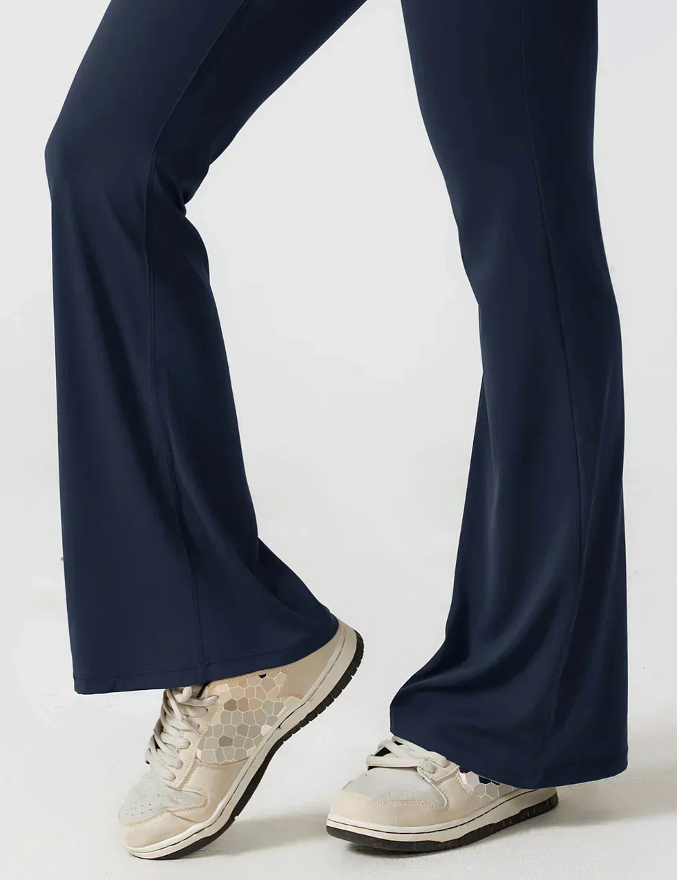 Person iført mørkeblå yogabukser og hvide sneakers. Fokus på benene i bevægelse. Komfortabelt sportstøj til træning og afslapning.