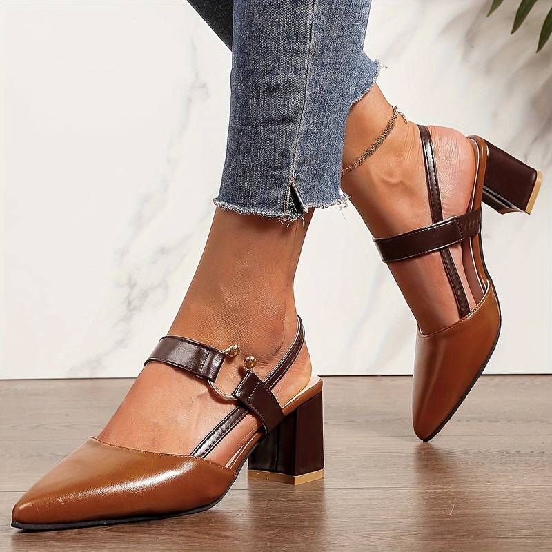 Brune læderpumps med blokhæl og rem, bæres af person i blå jeans. Moderne damesko, stilfuldt design, perfekt til hverdagsbrug og modebevidste kvinder.