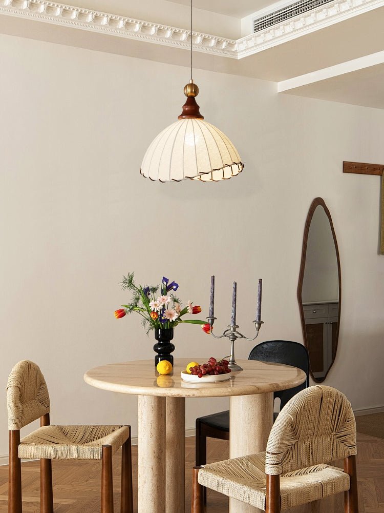 Rundt marmorbord med blomsterbuket, frugt og lysestager i moderne spisestue. Hængelampe og flettede stole tilføjer skandinavisk designstil.