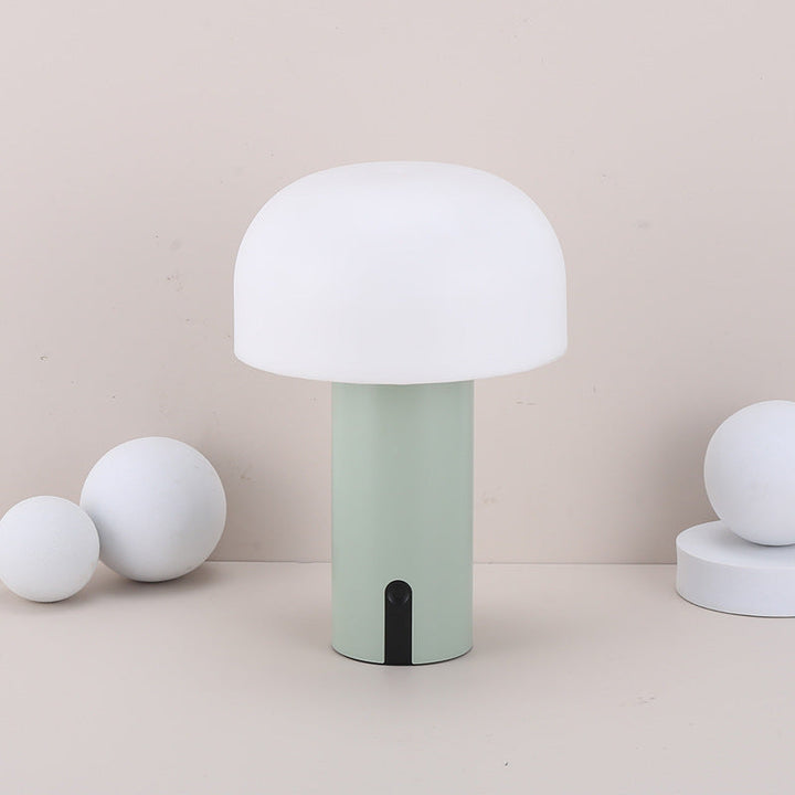 Moderne svampeformet bordlampe i minimalistisk design med hvid skærm og grøn base, omgivet af dekorative hvide kugler på beige baggrund.