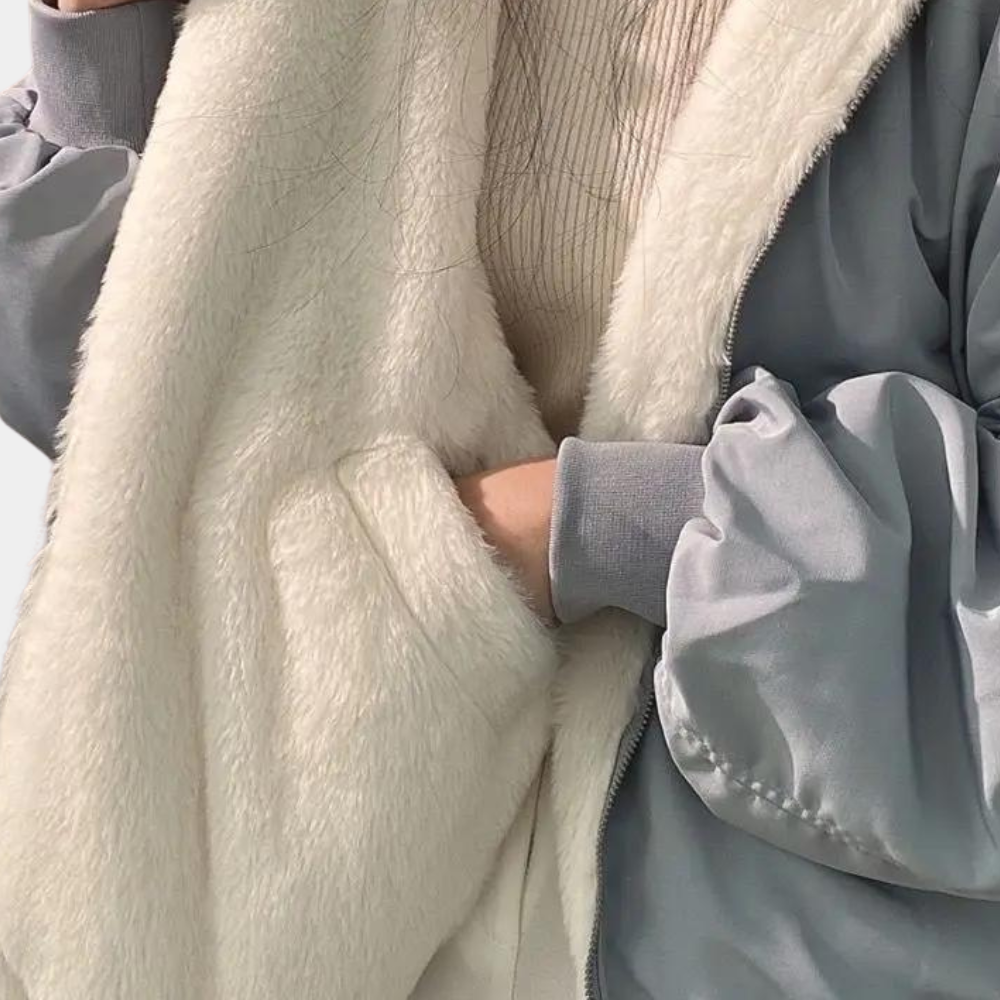 Grå jakke med hvidt plysfor, bæres af person i beige sweater. Vintermode, varm jakke, stilfuldt overtøj, komfortabelt design.