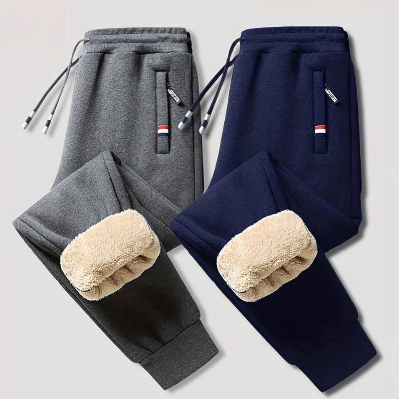 To par fleeceforede joggingbukser i grå og navy, med snøre og lynlåslommer. Komfortable og varme bukser til mænd, ideelle til vinterbrug.