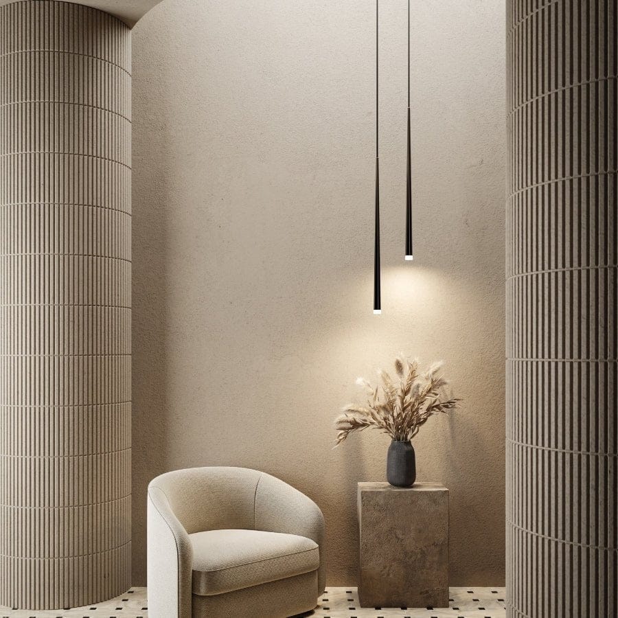 Moderne minimalistisk interiør med beige lænestol, vase med tørrede blomster på piedestal og slanke hængelamper mellem rillede søjler.