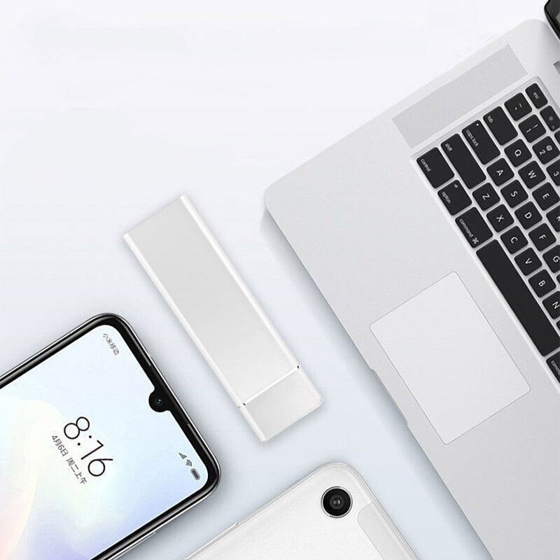Sølv USB-flashdrev ved siden af en bærbar computer og smartphone på et hvidt skrivebord. Moderne teknologi, dataopbevaring, minimalistisk design.