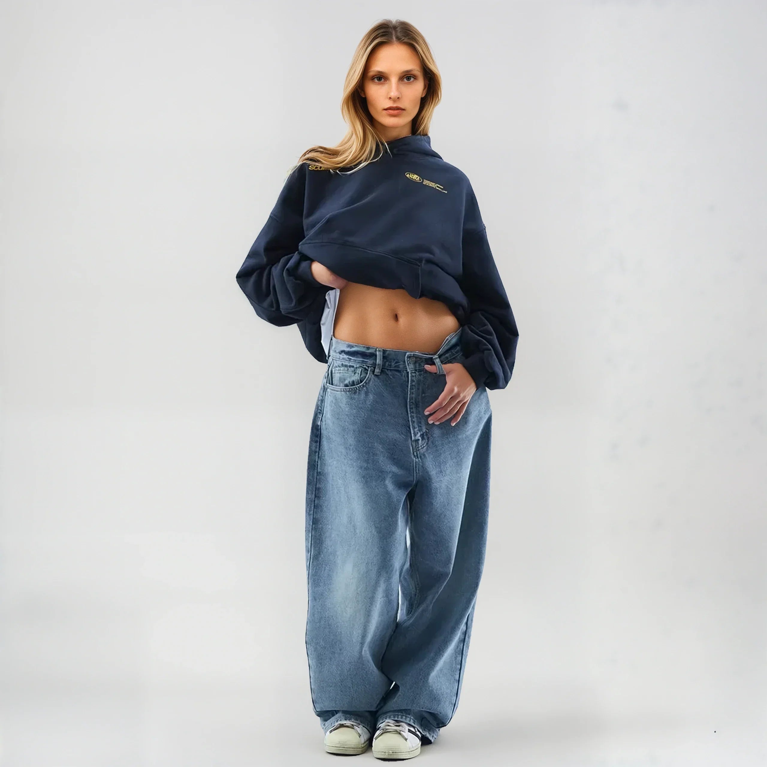 Ung kvinde i mørk sweatshirt og løse jeans, poserer i moderne streetwear-stil. Mode, afslappet tøj, trendy look, ungdommelig stil.