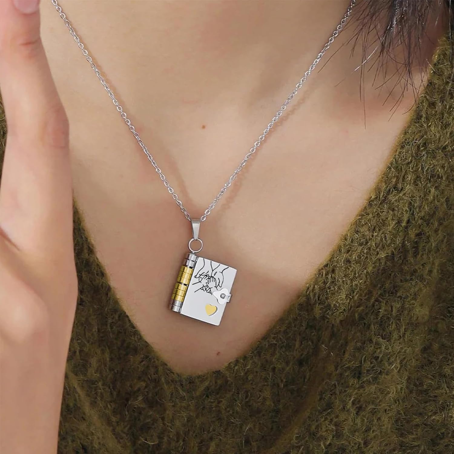 Sølvhalskæde med bogvedhæng, minimalistisk design, kvindehals, grøn trøje, moderne smykke, elegant tilbehør, unikt guld- og sølvdetaljer.