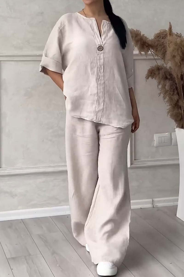 Kvinde iført beige linned sæt med kortærmet skjorte og vide bukser, stående på trægulv. Moderne minimalistisk tøjstil.