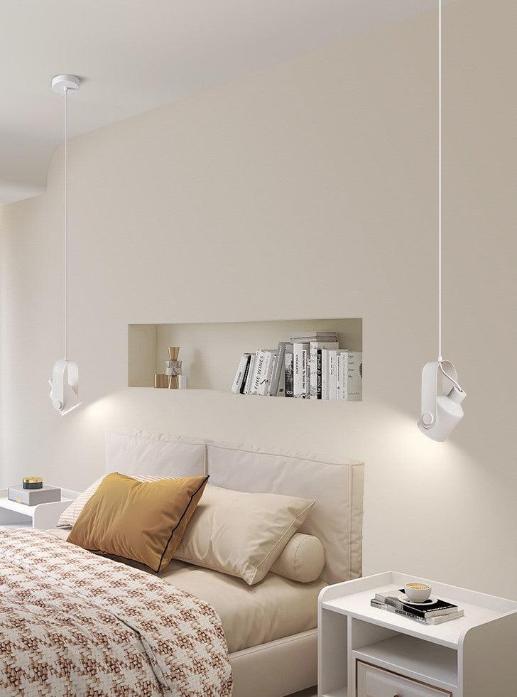 Moderne soveværelse med minimalistisk design, hvid seng, beige sengetøj, væghylde med bøger, og stilfulde hængelamper. Skandinavisk indretning.