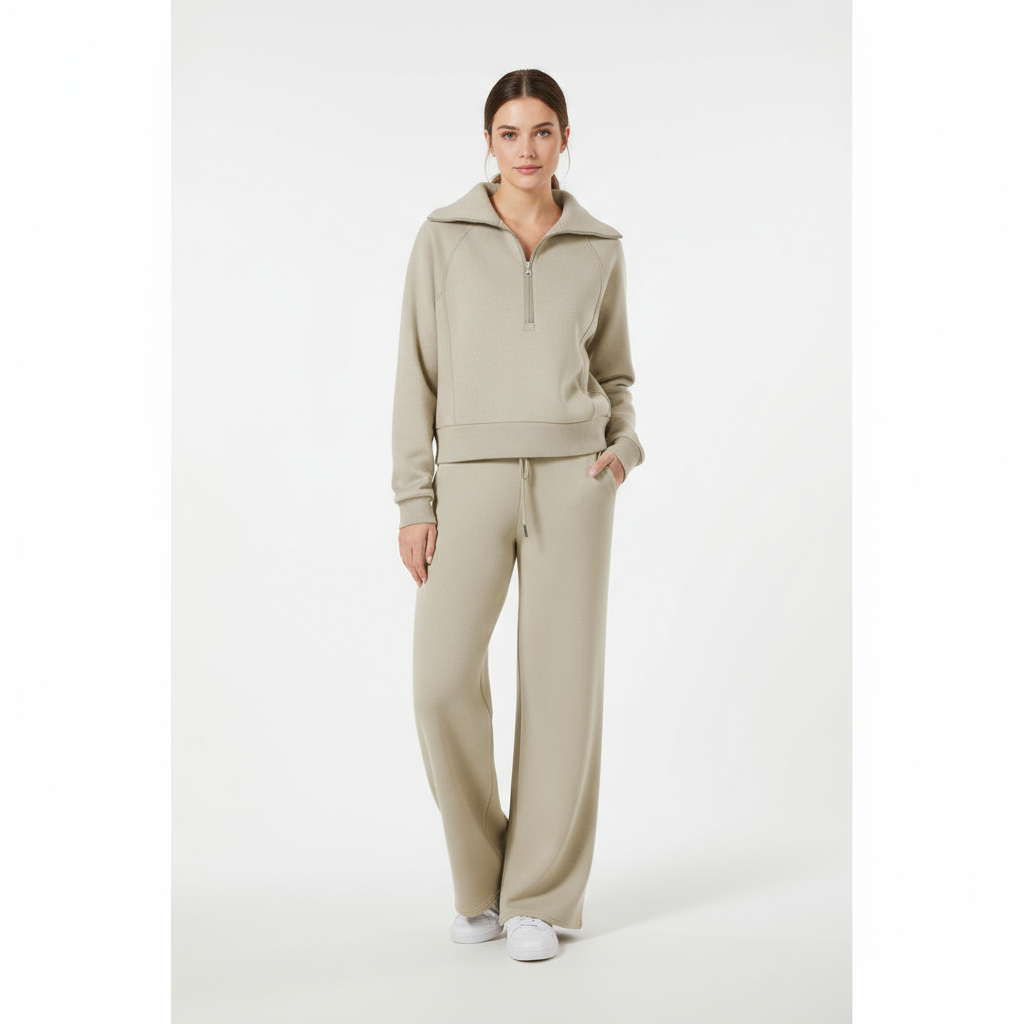 Kvinde iført beige joggingsæt med lynlås og hætte, poserer mod hvid baggrund. Komfortabelt loungewear, moderne afslappet stil, mode 2023.
