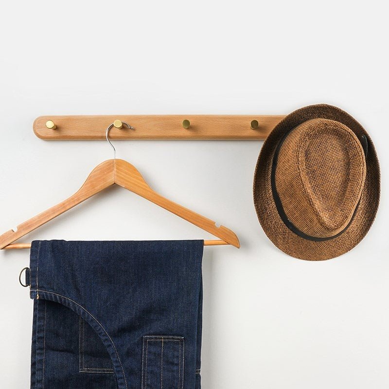 Brun stråhat og blå denimjeans hænger på træknagerække. Moderne indretning, minimalistisk design, praktisk opbevaring.
