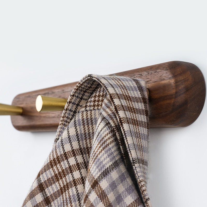 Brun træknage med gyldne kroge, der holder et ternet tørklæde. Elegant og funktionel opbevaringsløsning til entré eller garderobe.