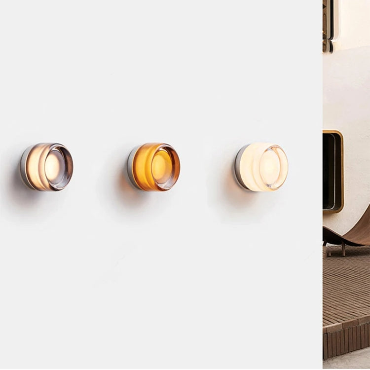 Tre moderne væglamper i forskellige nuancer af brun og hvid på en hvid væg. Stilfuldt belysningsdesign til indendørs brug.