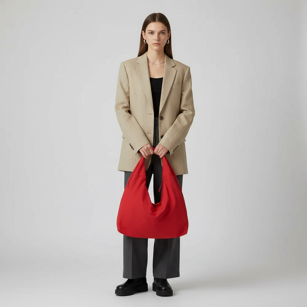 Kvinde i beige blazer og grå bukser holder en rød taske. Moderne mode, minimalistisk stil, elegant tilbehør, trendy outfit.