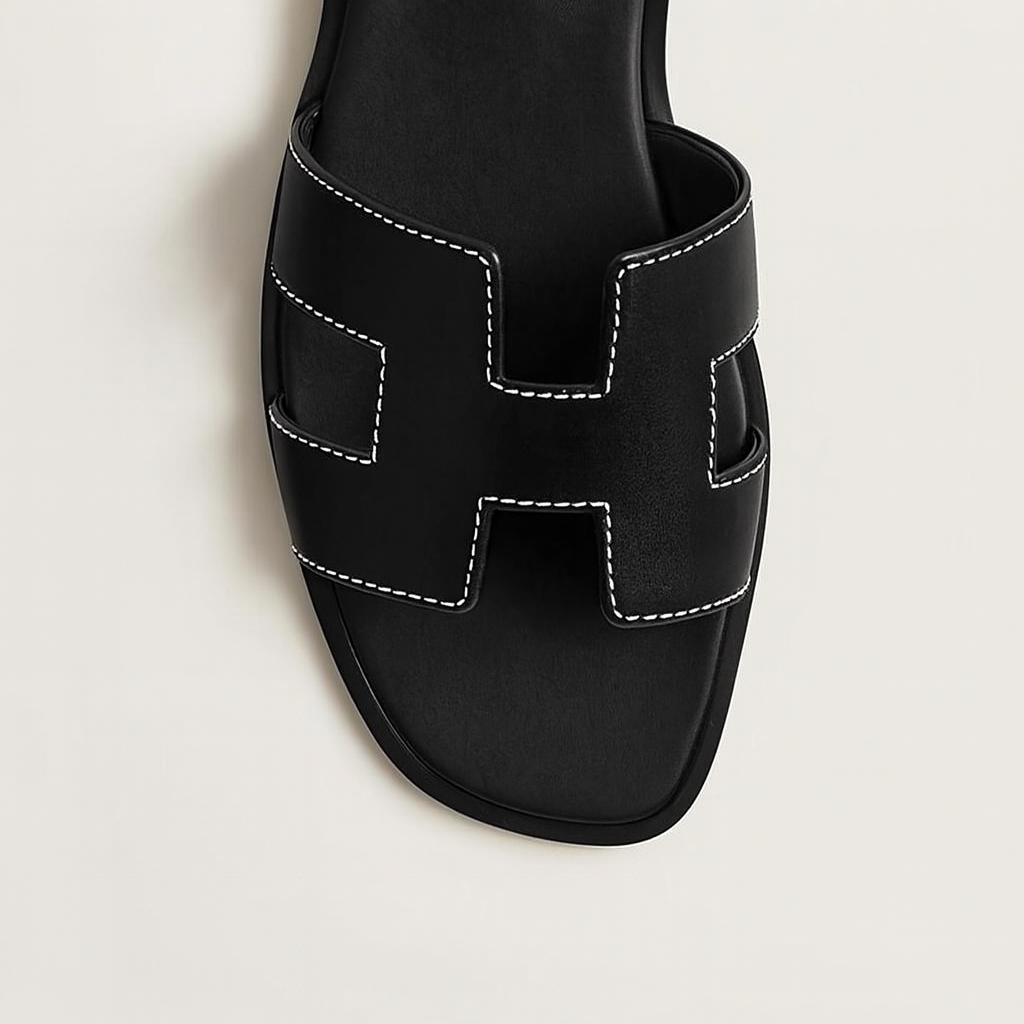 Sort lædersandal med hvid syning og H-formet rem. Elegant og moderne design, perfekt til sommermode. Komfortabel og stilfuld fodtøj.
