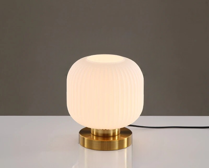 Moderne bordlampe med hvid, rillet glasskærm og gylden metalbase. Stilfuldt design til stue eller kontor. Energibesparende belysning.
